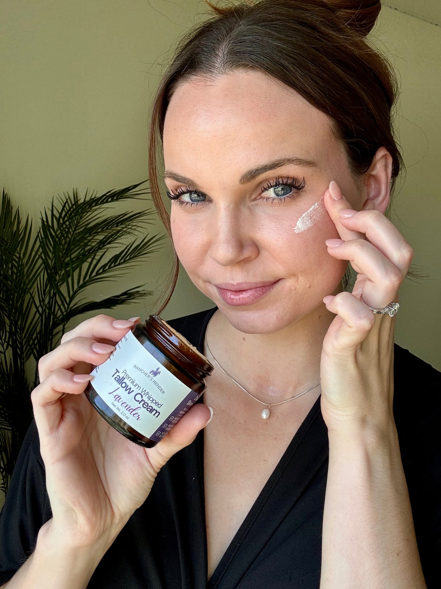 Woman applying ranchers render whipped tallow cream to her face with a jar of the same cream in her hand.