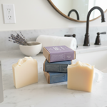 Three bars of soap on a marble countertop with a stack of boxes behind them.