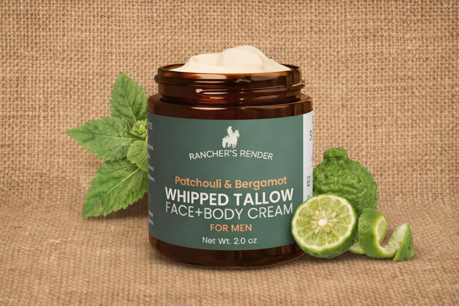 An amber glass jar of Rancher's Render Whipped Tallow Face & Body Cream for men, shown open with white cream on top, set on a burlap background with green patchouli and bergamot leaves and lime slices.
